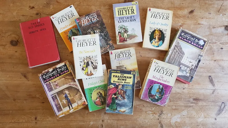 A dozen-ish romance books, all by Georgette Heyer, spread on a wooden surface.