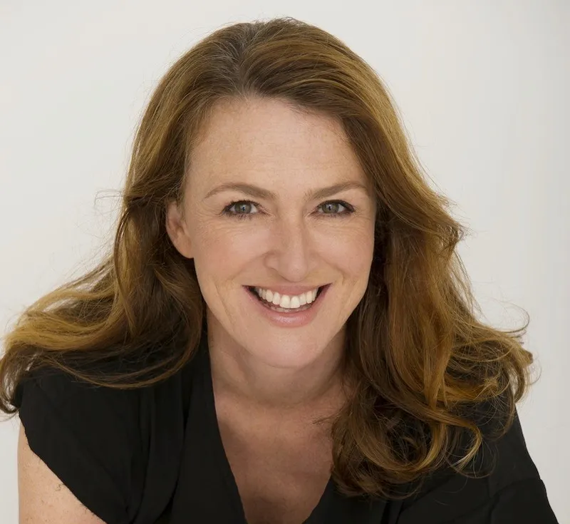 Head and shoulders photograph of middle-aged woman with big smile and loads of beautiful chestnut hair.