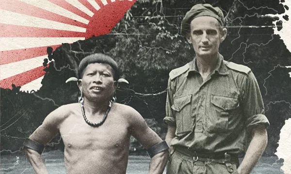 Black and white photograph showing two men, one shorter in indigenous Borneo dress, one tall skinny Pākeha in military dress. Design element of red rising sun has been added to the background.
