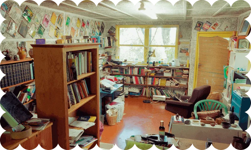 Photograph of a full-to-bursting room, books and papers and shelves everywhere, even the wallpaper is busy. No people.