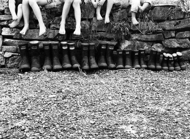 Black and white photo of eight pairs of Red Bands lined up against a wall. Above each pair, you can see a child sitting, legs dangling.