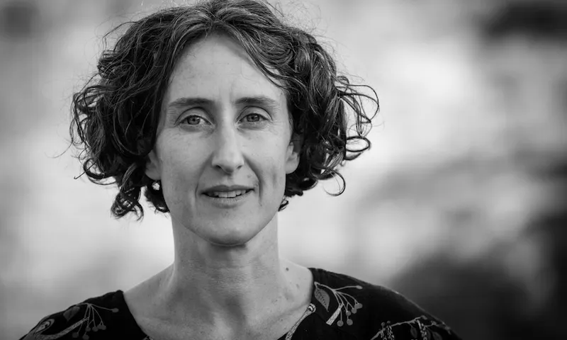 Black and white portrait photograph of a middle-aged woman with curly hair, looking to camera.