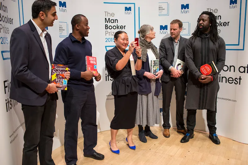 Six writers arranged in front of the Man Booker Prize posters. Photo taken at a candid moment, the shorter woman in the middle (Hanya Yanagihara) is taking a selfie.