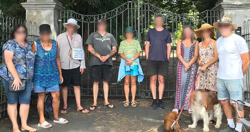 A group of individuals standing in front of the gates to Government House