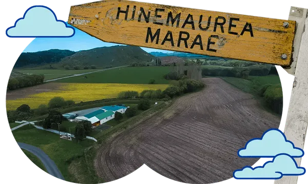 A wooden sign reading "HINEMAUREA MARAE" stands above a rural landscape with fields, a building, hills, and illustrated blue clouds decorating the image.