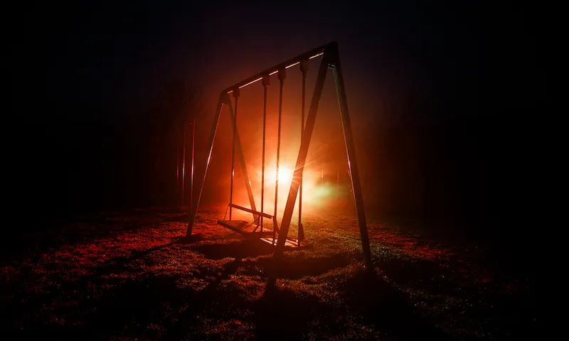 Night photo of metal swing with car light behind