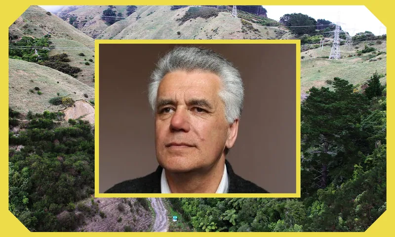 A portrait of an older man with gray hair is centered within a yellow border. The background shows green, hilly terrain with trees and power lines, also framed by a yellow border.