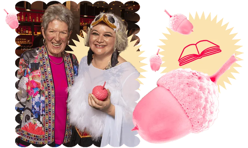 Photograph of two very happy women, one holding a trophy in the shape of a pink acorn. Other pink acorns are zooming around as design elements, with book emojis.