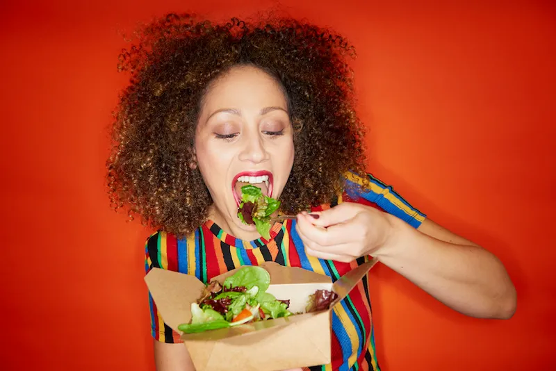 Woman laughing as she eats salad, red background