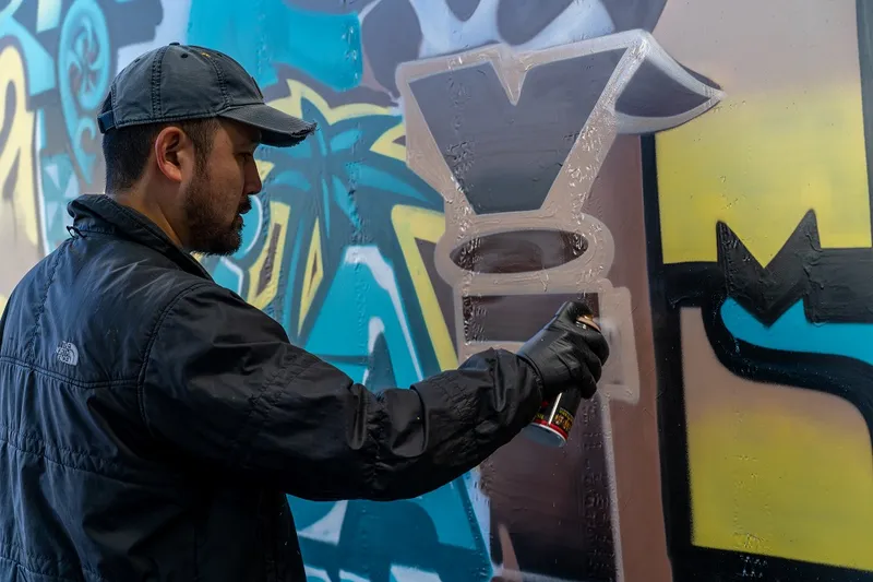 Bobby Hung, wearing a black cap and jacket, ads the finishing touches to a blue and yellow mural