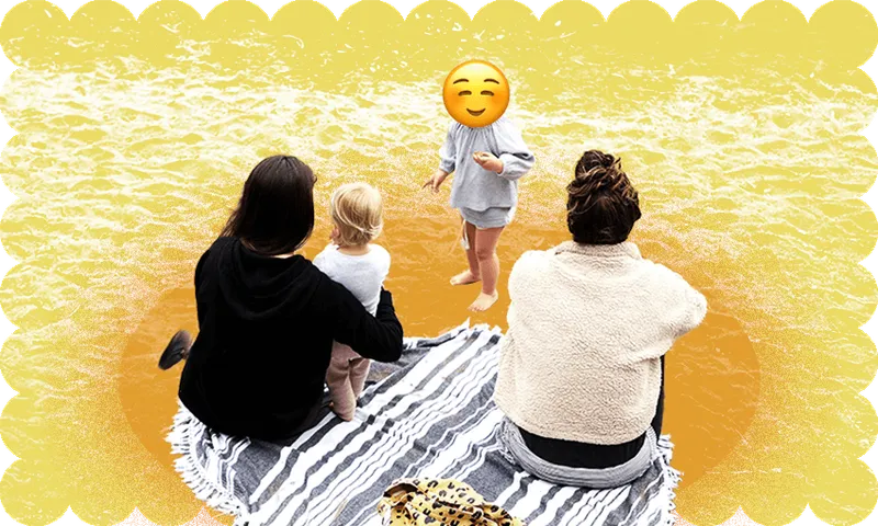 a family has a picnic on the beach. one child is shown with only the back of their head visible; one child has a smiling emoji over their face