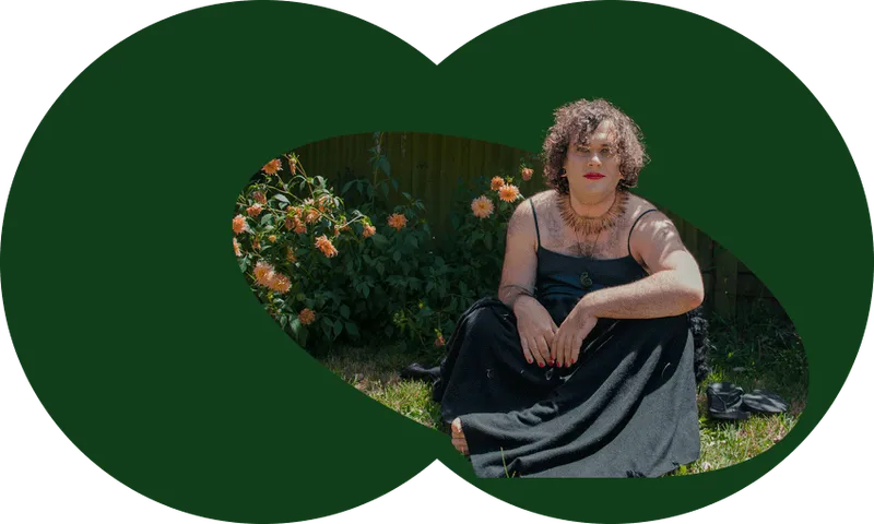 Photo shows the author sitting in a garden, wearing a long black dress with spaghetti straps. Orange dahlias and purple wisteria behind.