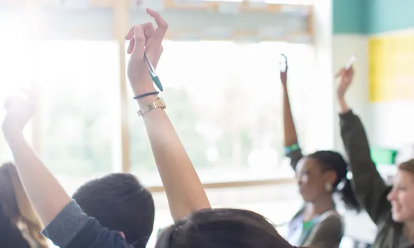 Teenage students with arms raised in classroom