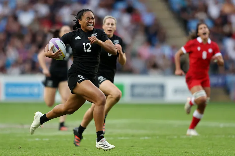 Photo of a woman grimacing as she races with ball in hand, other players in her wake.