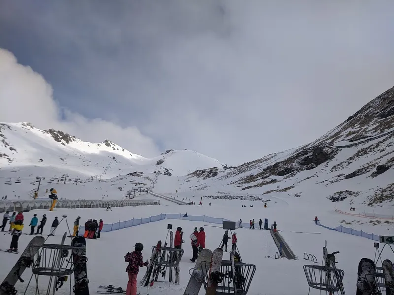 lots of skiiers and snowboarders clusterd in foreground with mountain and lifts in background