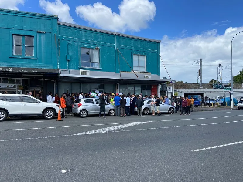 blue sky blue/teal building two police cars and people milling on the road