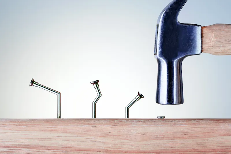 Three bent nails and a hammer driving a fourth in straight