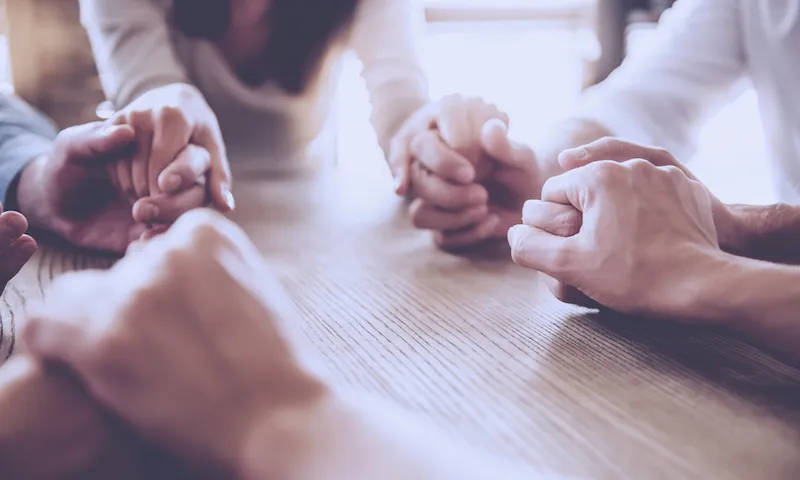 close up of people holding hands and praying