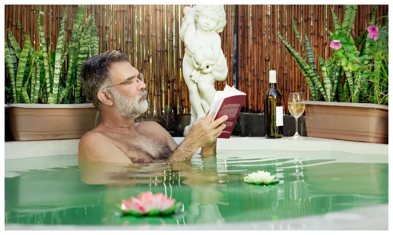 Mature man in bath with waterlilies and wine, reading a book