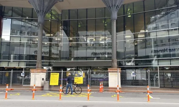 Exterior of Wellington Central Library, featuring temporary fencing, roadcones and a cyclist