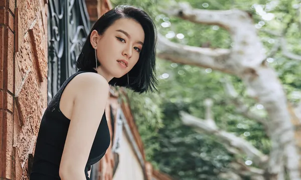 A photograph of Chloe Gong, looking to camera, with trees in the background
