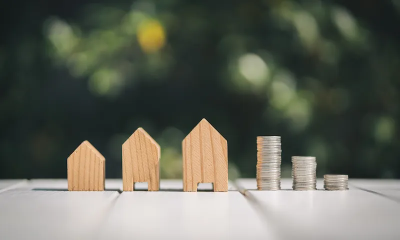 Close-Up Of Wooden Model Homes And Stacked Coins On Table