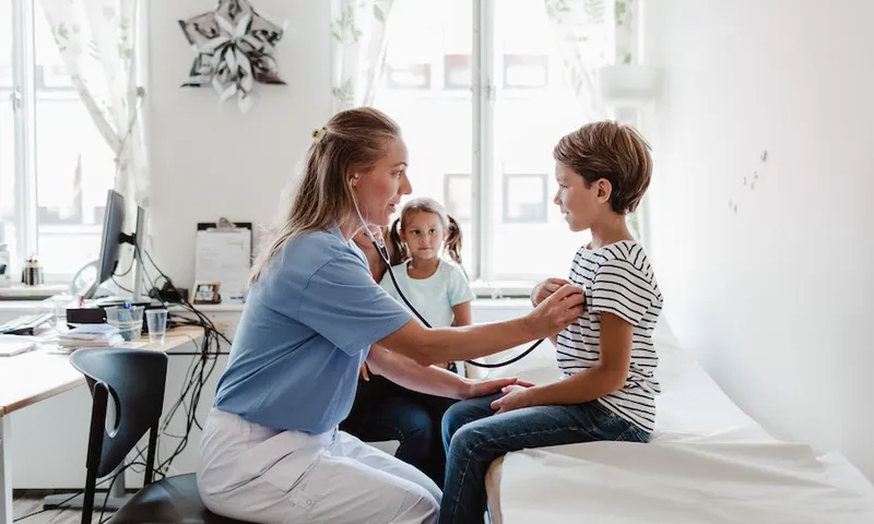 Female doctor listening to boy's heartbeat while family sitting in medical room