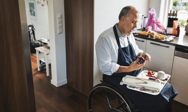 Disabled man in wheelchair cutting onion at kitchen