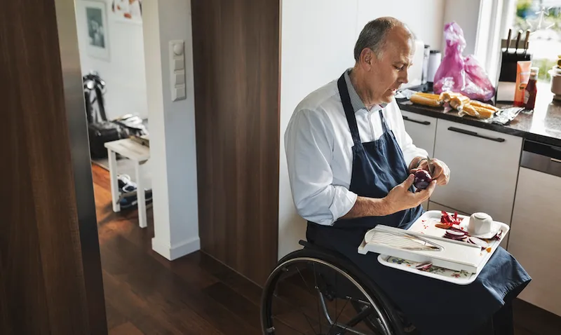 Disabled man in wheelchair cutting onion at kitchen