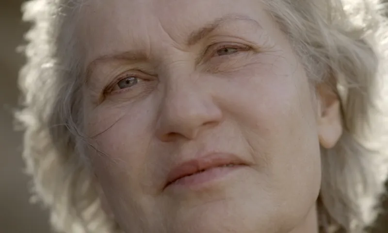 Close-up photograph of a senior woman looking straight to camera, in natural light