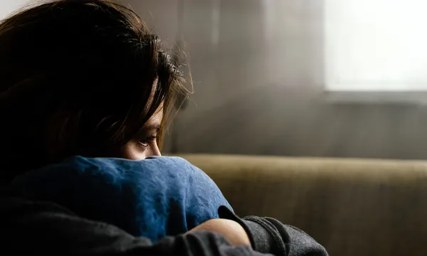 Close-Up Of Sad Woman Hugging Cushion While Sitting At Home