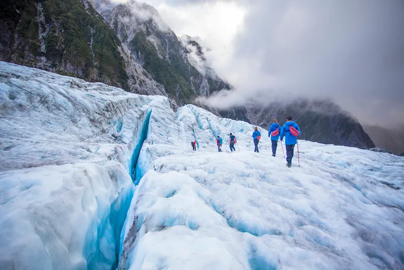 Travelers explore New Zealand's famous Franz Josef Glacier. Blue Ice, deep crevasses, caves and tunnels mark the ever changing ice.