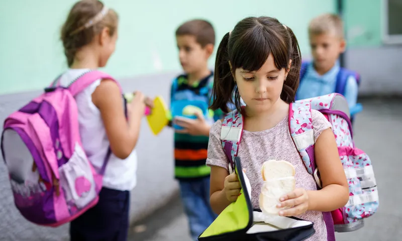 Little girl holding lunch box and eating sandwich