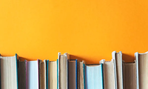 A bright orange wall, along the bottom of the photograph we see old books, stacked spine-down.