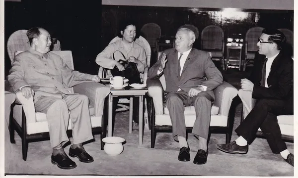 An old black and white photograph showing four people in a formal meeting,