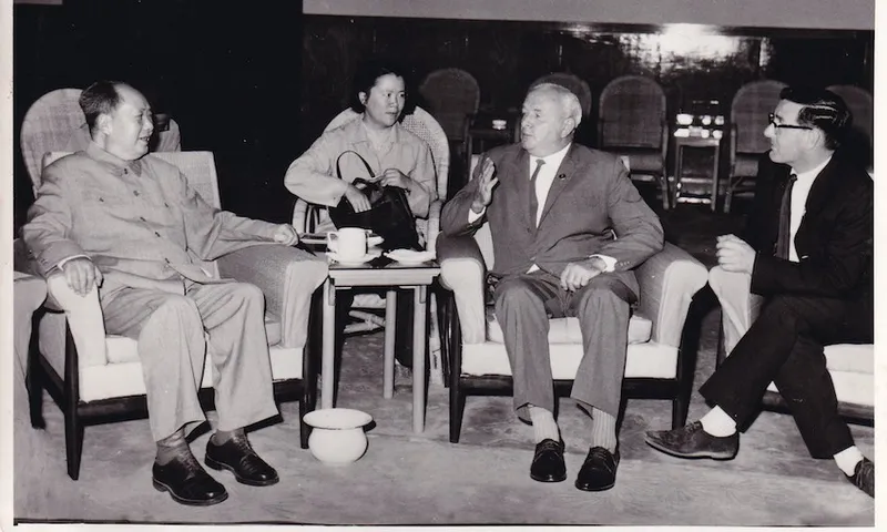 An old black and white photograph showing four people in a formal meeting,