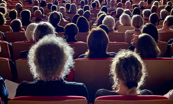 We're in a dimly-lit auditorium, looking at rows and rows of heads in the audience in front of us.