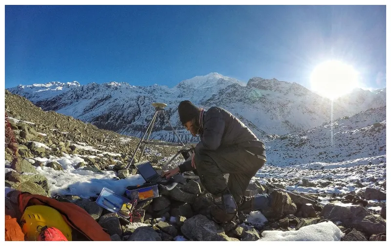 Young man adjusts scientific equipment in the bedrock of the Haupapa glacier. Beautiful clear day.