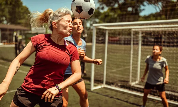 Female soccer striker heads ball into the goal