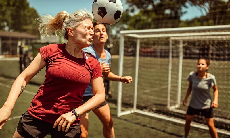 Female soccer striker heads ball into the goal