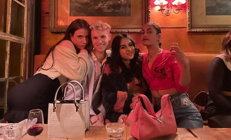 Four friends posing on a couch at a bar. Scene tinged with pink from the lights.