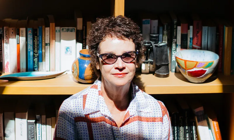 Photograph of a middle-aged woman sitting in front of a sunlit bookcase.