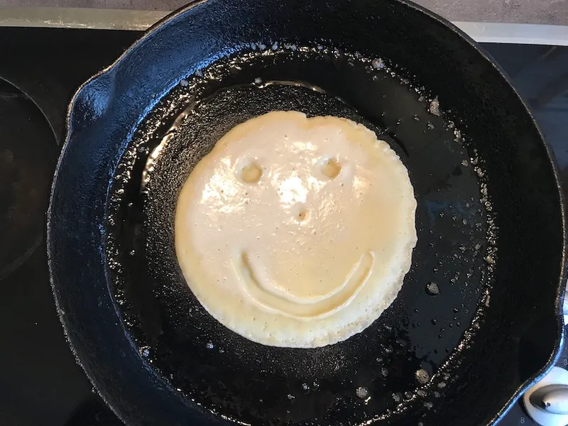 Pancake cooking in cast-iron pan, smily face in batter