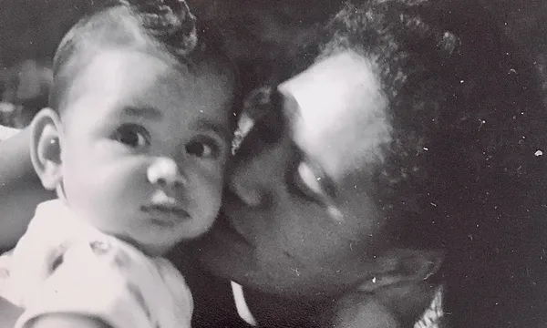 Old black and white family photo, very beautiful, a mother kissing her baby's cheek. Baby looking straight to camera.