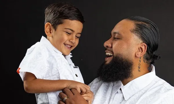 A father holds his son, both delighted, on his son's sixth birthday. Both wearing collared white shirts.