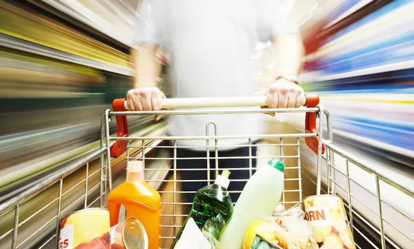 Speed blurs male shopper in supermarket with full shopping cart