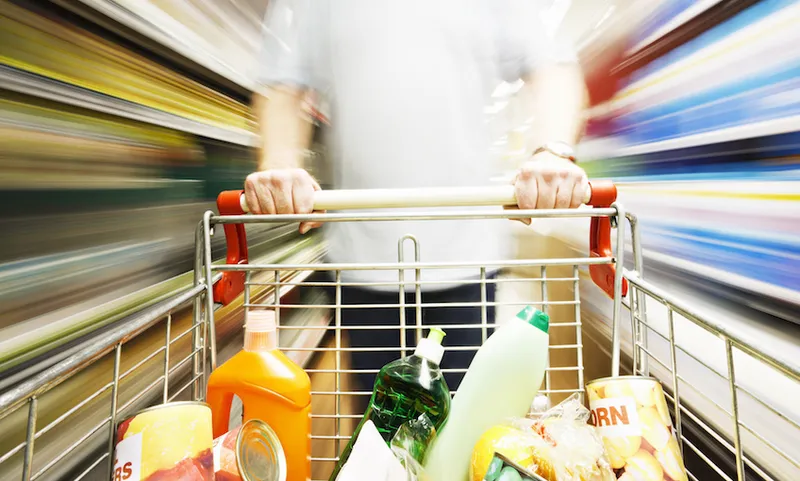Speed blurs male shopper in supermarket with full shopping cart