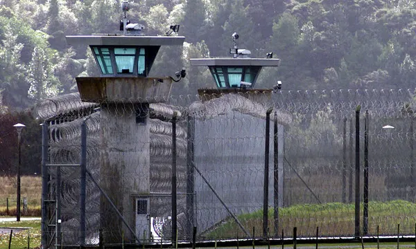 Exterior view of a prison yard and guard towers, backdrop of native bush