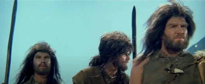 Still from an old film showing three actors dressed as Neanderthals. Terrible wigs.