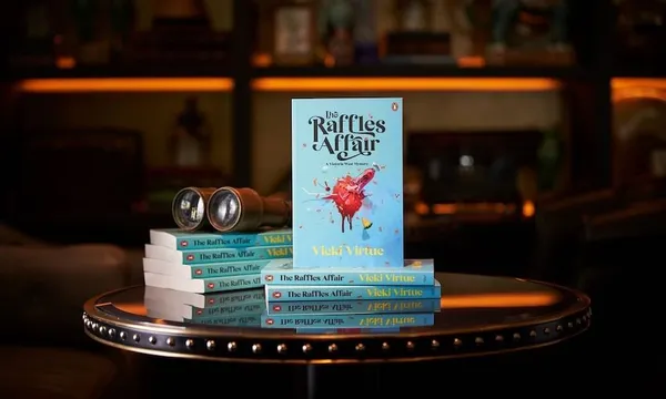 Photo of a pile of books, one stood up so we can see the cover. Setting is a gloomy library.